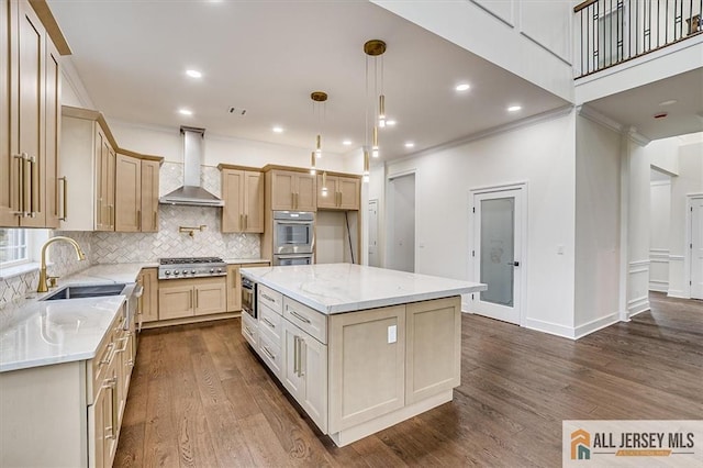 kitchen featuring appliances with stainless steel finishes, sink, a center island, wall chimney range hood, and light stone countertops