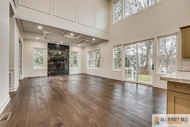 unfurnished living room featuring coffered ceiling, dark hardwood / wood-style floors, plenty of natural light, and a premium fireplace