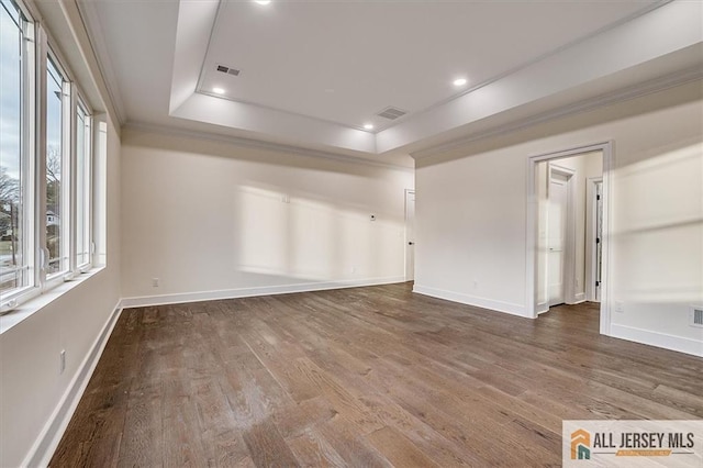 empty room with wood-type flooring, a tray ceiling, and ornamental molding