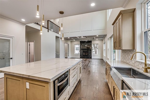 kitchen with a large island, hanging light fixtures, sink, oven, and wood-type flooring