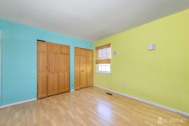 unfurnished bedroom featuring multiple closets and light hardwood / wood-style flooring