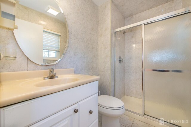 bathroom with tile walls, toilet, a shower with door, and vanity