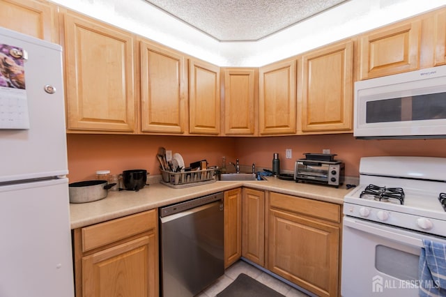 kitchen with a textured ceiling, light brown cabinets, white appliances, a sink, and light countertops