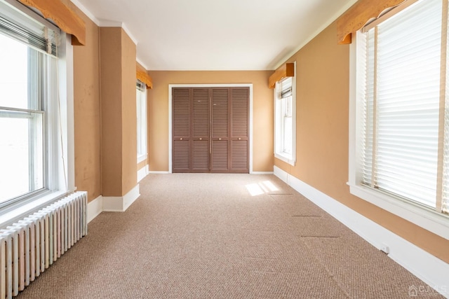 unfurnished bedroom with multiple windows, a closet, radiator heating unit, and light carpet