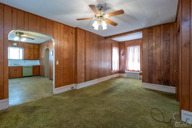 carpeted spare room featuring radiator, ceiling fan, and wood walls