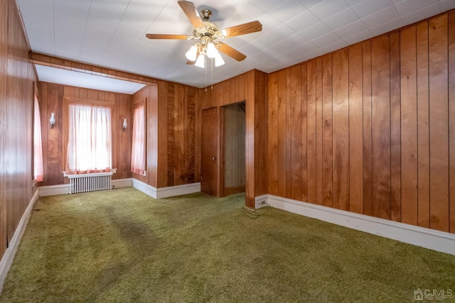 unfurnished room featuring ceiling fan, wood walls, radiator heating unit, and carpet floors