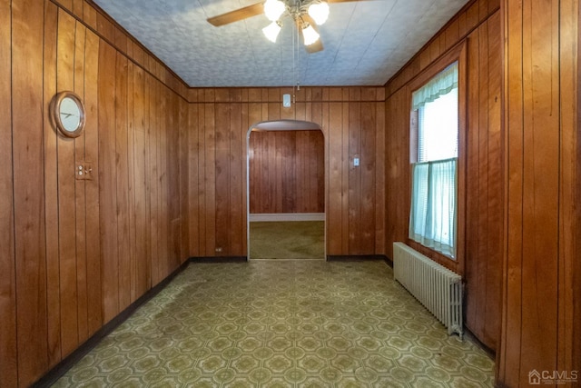 spare room featuring ceiling fan, wood walls, and radiator heating unit