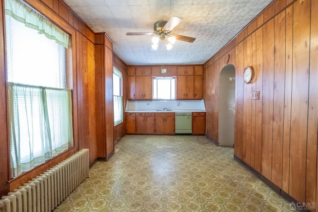 kitchen with dishwasher, sink, wooden walls, ceiling fan, and radiator heating unit