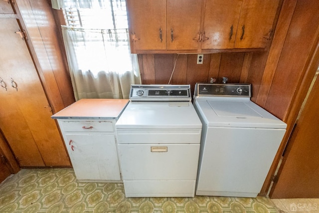 clothes washing area featuring washer and dryer, cabinets, and wood walls