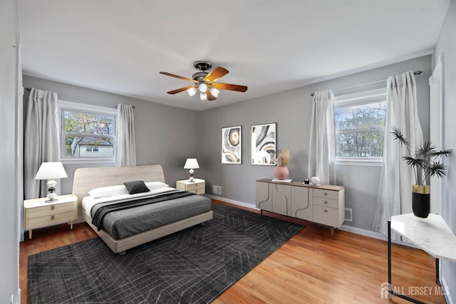 bedroom with baseboards, ceiling fan, multiple windows, and wood finished floors