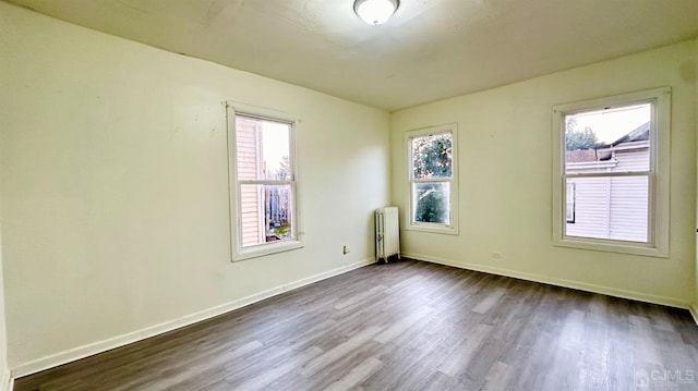 empty room with dark wood-style flooring, baseboards, and radiator heating unit