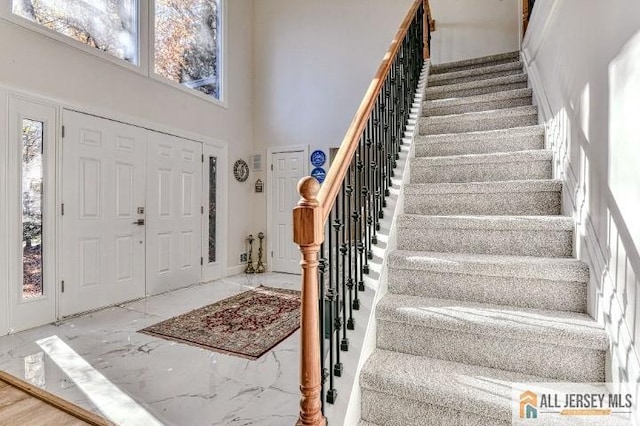 foyer featuring marble finish floor, stairs, and a high ceiling