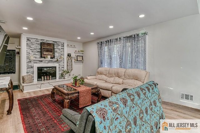 living room featuring a large fireplace, visible vents, wood finished floors, and recessed lighting