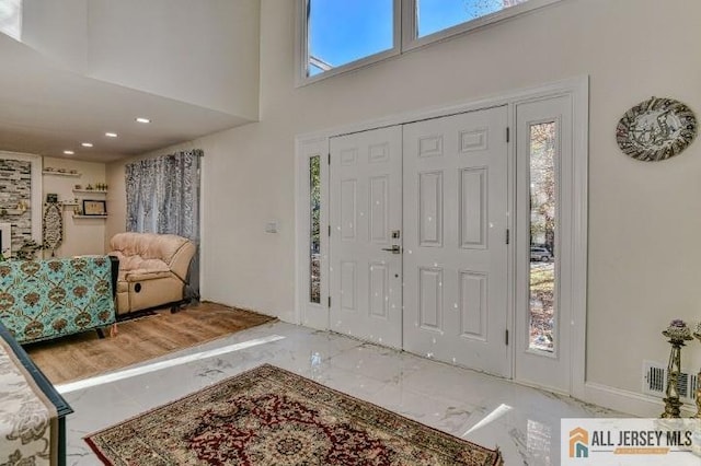 entrance foyer with a wealth of natural light, marble finish floor, visible vents, and a towering ceiling