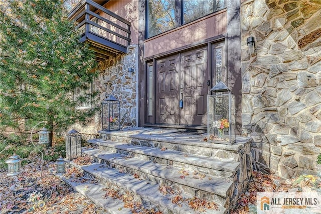 entrance to property featuring stone siding and a balcony