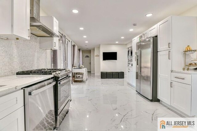 kitchen with light stone counters, marble finish floor, stainless steel appliances, white cabinets, and wall chimney exhaust hood