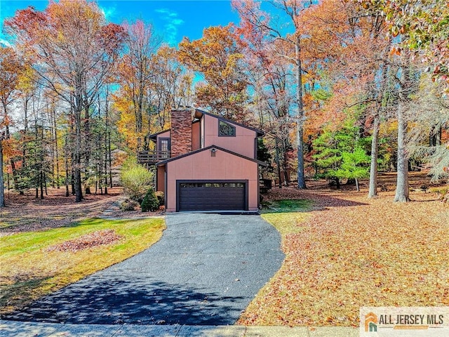 view of front facade with aphalt driveway, a chimney, and an attached garage