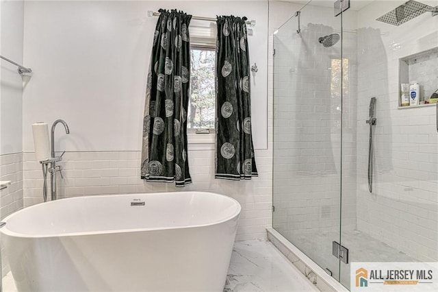 bathroom featuring marble finish floor, a freestanding tub, tile walls, and a shower stall