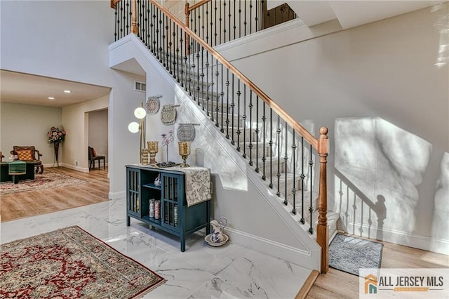 staircase featuring visible vents, marble finish floor, a towering ceiling, and baseboards