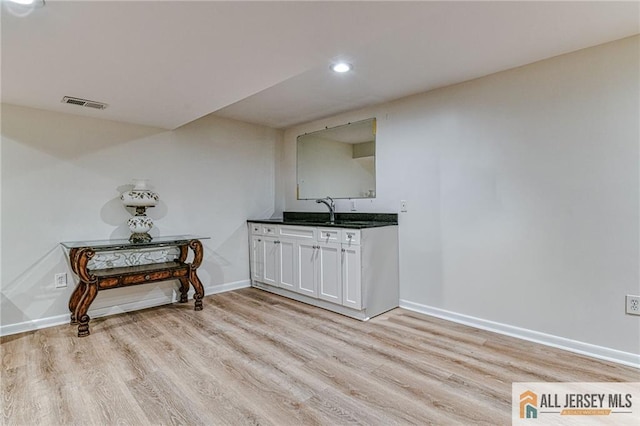 kitchen with baseboards, white cabinets, dark countertops, light wood-style flooring, and a sink