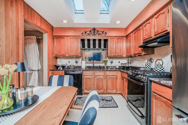 kitchen featuring a skylight, a sink, black appliances, under cabinet range hood, and brown cabinets