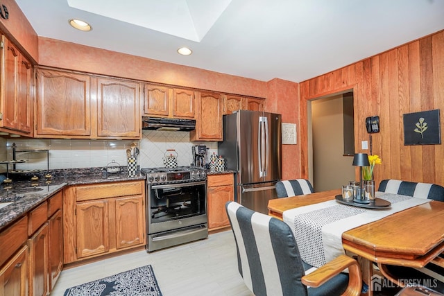 kitchen with brown cabinetry, a skylight, stainless steel appliances, decorative backsplash, and under cabinet range hood