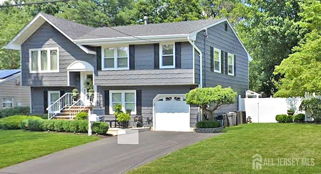 bi-level home featuring a front lawn, an attached garage, fence, and driveway