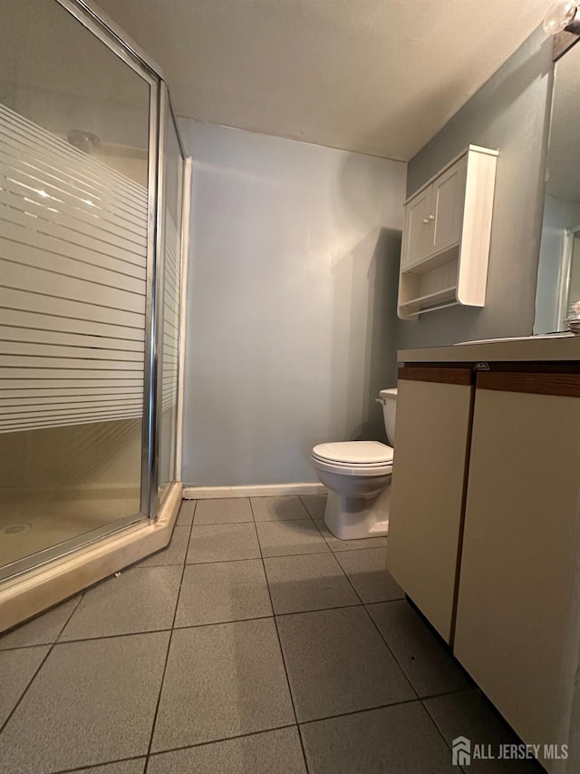 bathroom with tile patterned flooring, toilet, vanity, baseboards, and a stall shower