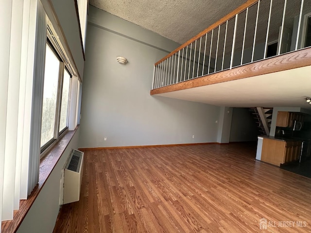 unfurnished living room featuring a wall unit AC, a high ceiling, baseboards, and wood finished floors