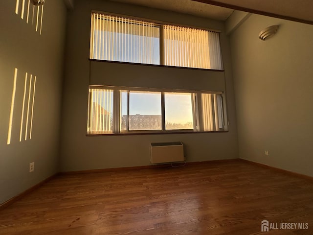 spare room with a high ceiling, wood finished floors, and heating unit