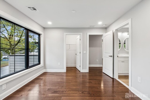 unfurnished bedroom featuring dark hardwood / wood-style flooring, a walk in closet, connected bathroom, and a closet