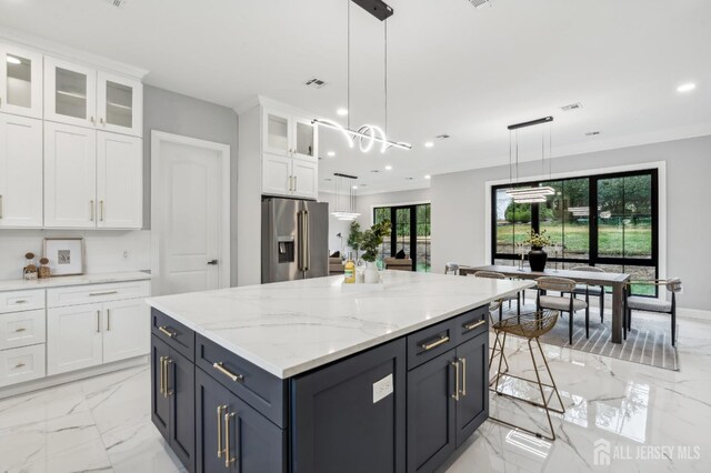 kitchen featuring pendant lighting, stainless steel fridge, a kitchen island, light stone counters, and white cabinetry