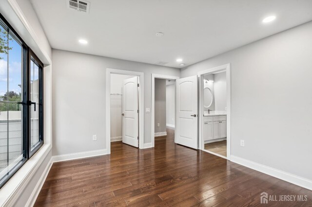 unfurnished bedroom featuring ensuite bathroom, a spacious closet, dark wood-type flooring, and a closet