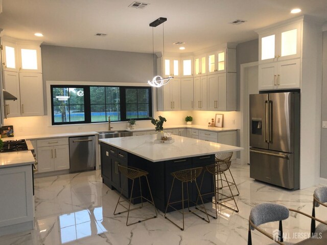 kitchen featuring white cabinetry, sink, decorative light fixtures, a kitchen island, and appliances with stainless steel finishes