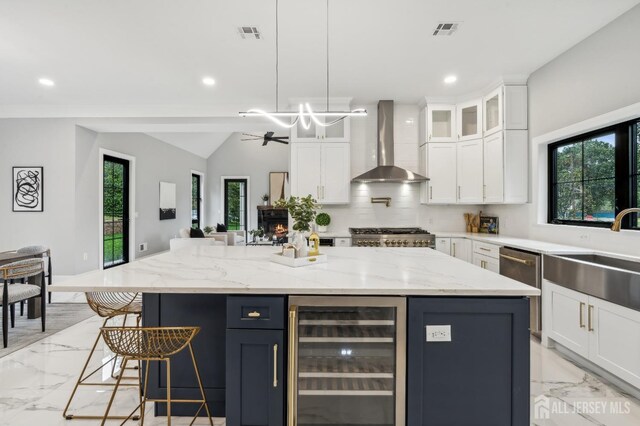 kitchen with wall chimney exhaust hood, a kitchen island, decorative light fixtures, and beverage cooler