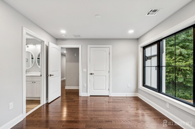 unfurnished bedroom with dark hardwood / wood-style flooring, multiple windows, and connected bathroom