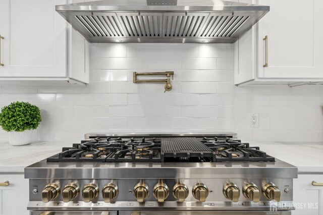 kitchen with white cabinetry, wall chimney range hood, and stainless steel stove