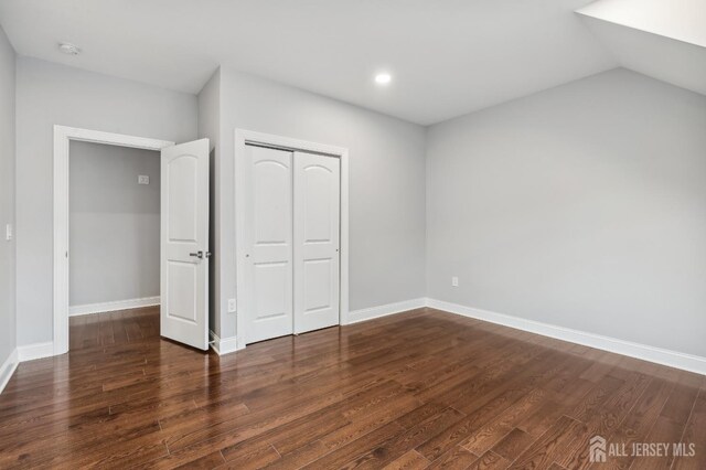 unfurnished bedroom featuring lofted ceiling, a closet, and dark hardwood / wood-style floors