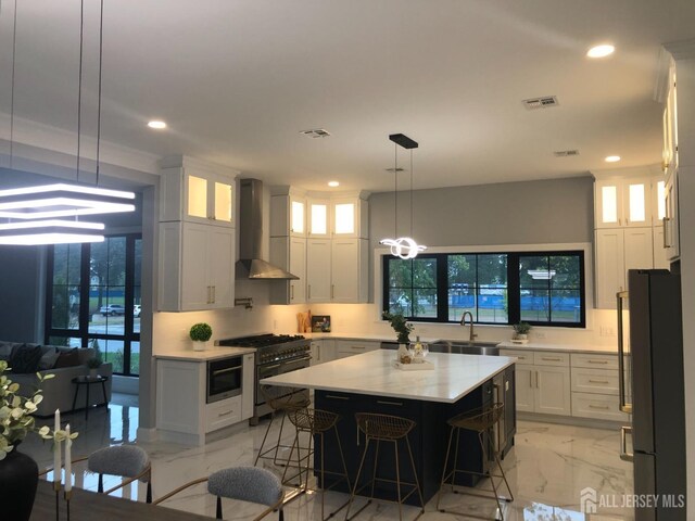 kitchen featuring a center island, stainless steel appliances, white cabinetry, and wall chimney exhaust hood