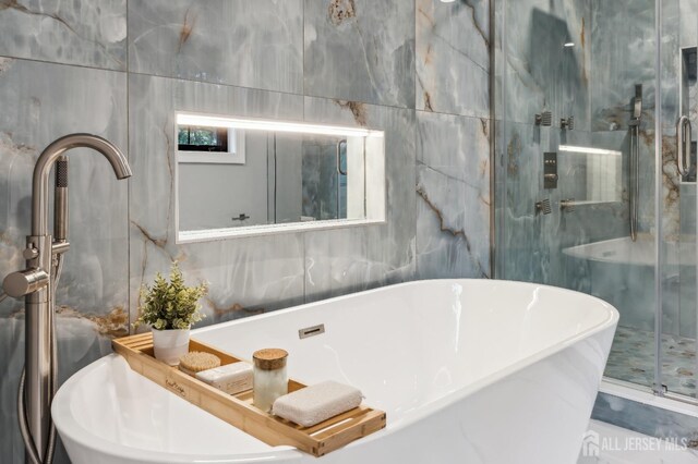 bathroom with shower with separate bathtub and tile walls