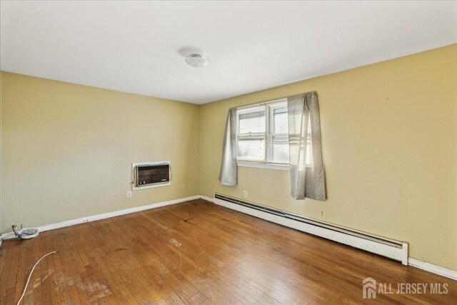 empty room with a wall mounted AC, a baseboard radiator, and hardwood / wood-style flooring