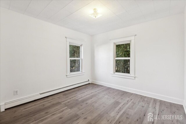 empty room featuring light hardwood / wood-style floors, a wealth of natural light, and a baseboard heating unit