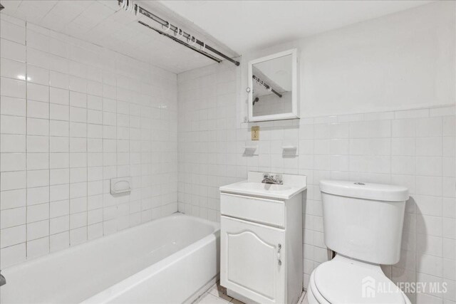 full bathroom featuring toilet, vanity, tile walls, and tiled shower / bath combo