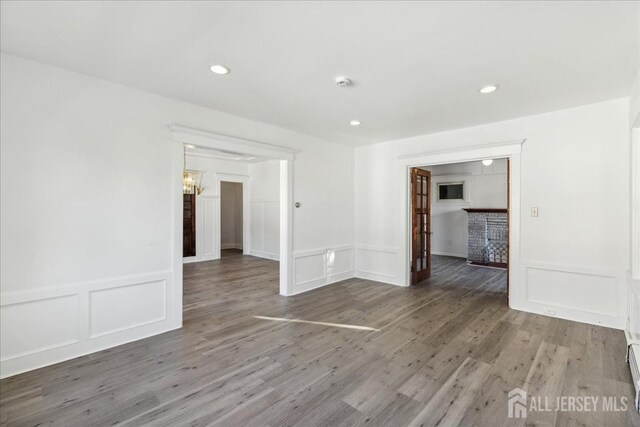 unfurnished room with a notable chandelier, baseboard heating, and hardwood / wood-style floors