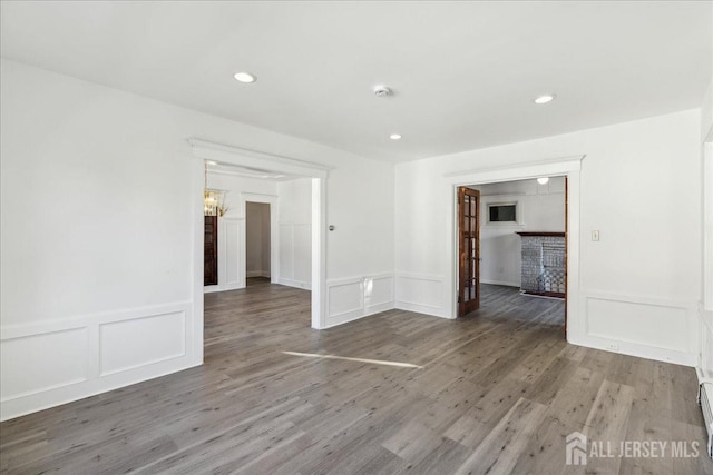 spare room featuring a chandelier, a baseboard heating unit, and hardwood / wood-style floors