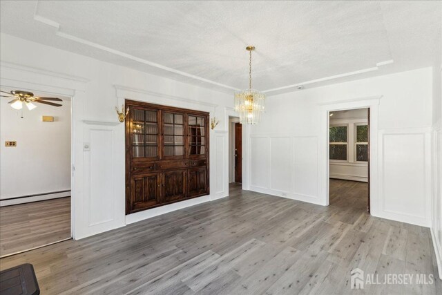 unfurnished dining area with a textured ceiling, a baseboard heating unit, ceiling fan with notable chandelier, and hardwood / wood-style flooring