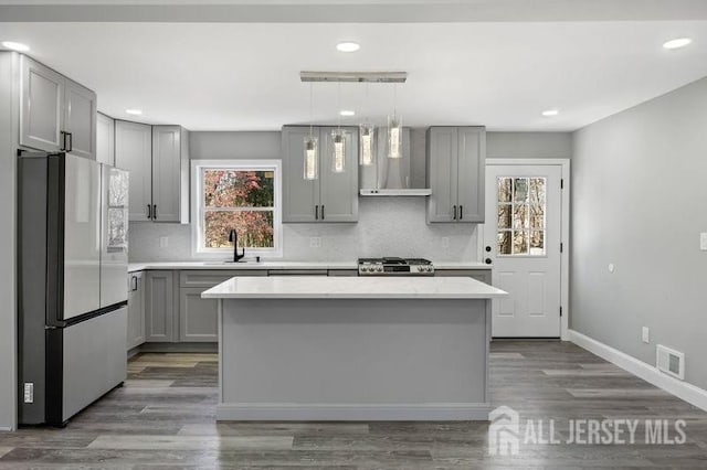 kitchen with decorative light fixtures, wall chimney exhaust hood, a kitchen island, and stainless steel refrigerator