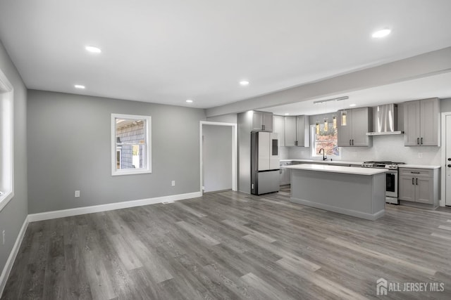 kitchen with appliances with stainless steel finishes, a center island, wall chimney exhaust hood, hanging light fixtures, and gray cabinetry