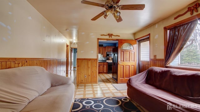 living area with wainscoting, ceiling fan, wooden walls, and light floors