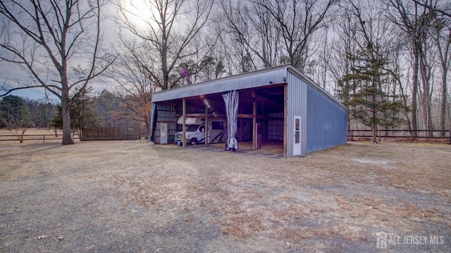 view of pole building with dirt driveway, a carport, and fence